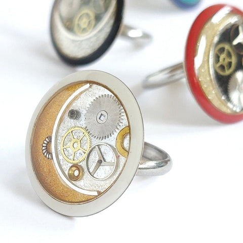 L'anello in resina oro, argento e nero, è decorato con  ingranaggi di orologi vintage. La base è una veretta anallergica, in acciaio, con misura regolabile. Leggero e comodo. Sicuro, grazie alla regolazione della misura, posizionata sulla parte superiore della mano, che evita l'effetto "pizzicotto". 